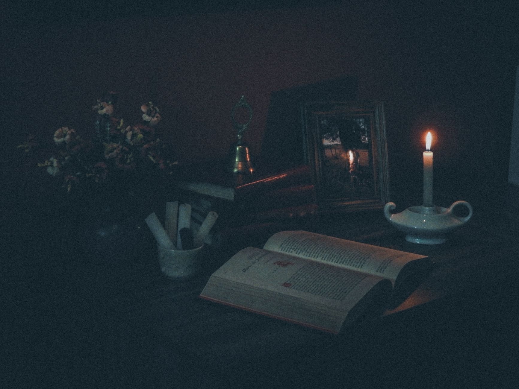 A dimly lit still life featuring an open book and a candle casting a warm glow