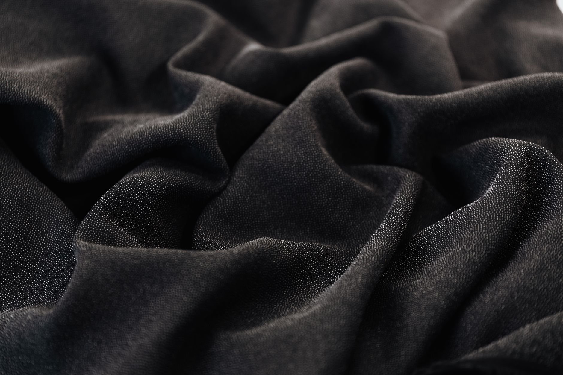 Black fabric with intricate folds and texture, suggesting depth and mystery